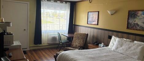 A hotel room with a bed, a desk with a lamp, a chair, a window with curtains, and two wall-mounted lamps.