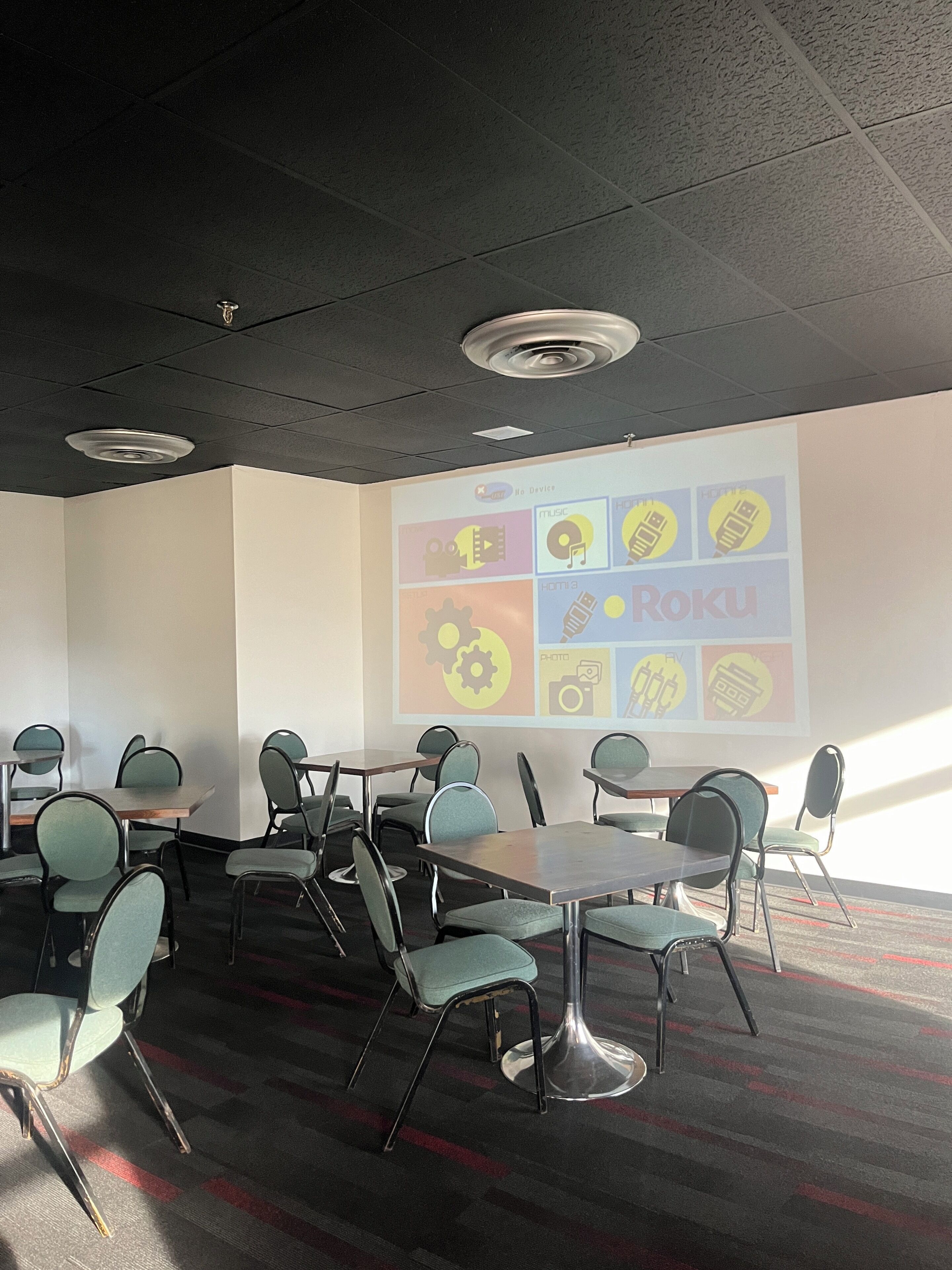 A conference room with a projector screen displaying icons, a table, and chairs.