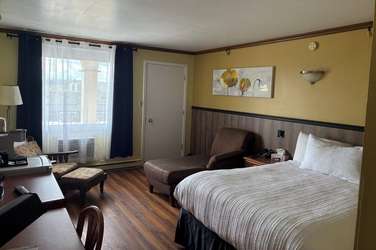 A hotel room with a bed, a chair, a desk, and a window with curtains.