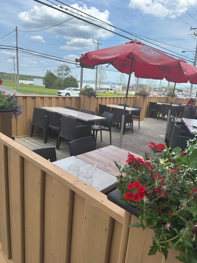 Un patio al aire libre con mesas y sillas de madera, sombrillas rojas y plantas en macetas.