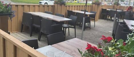 Une terrasse extérieure avec des tables et des chaises en bois, des parasols rouges et des plantes en pot.