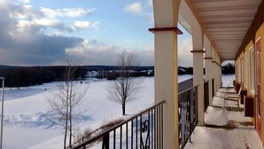 A covered porch with a view of a snowy landscape and a row of buildings in the background. - Hotel Motel Le Château (Lac-Megantic)