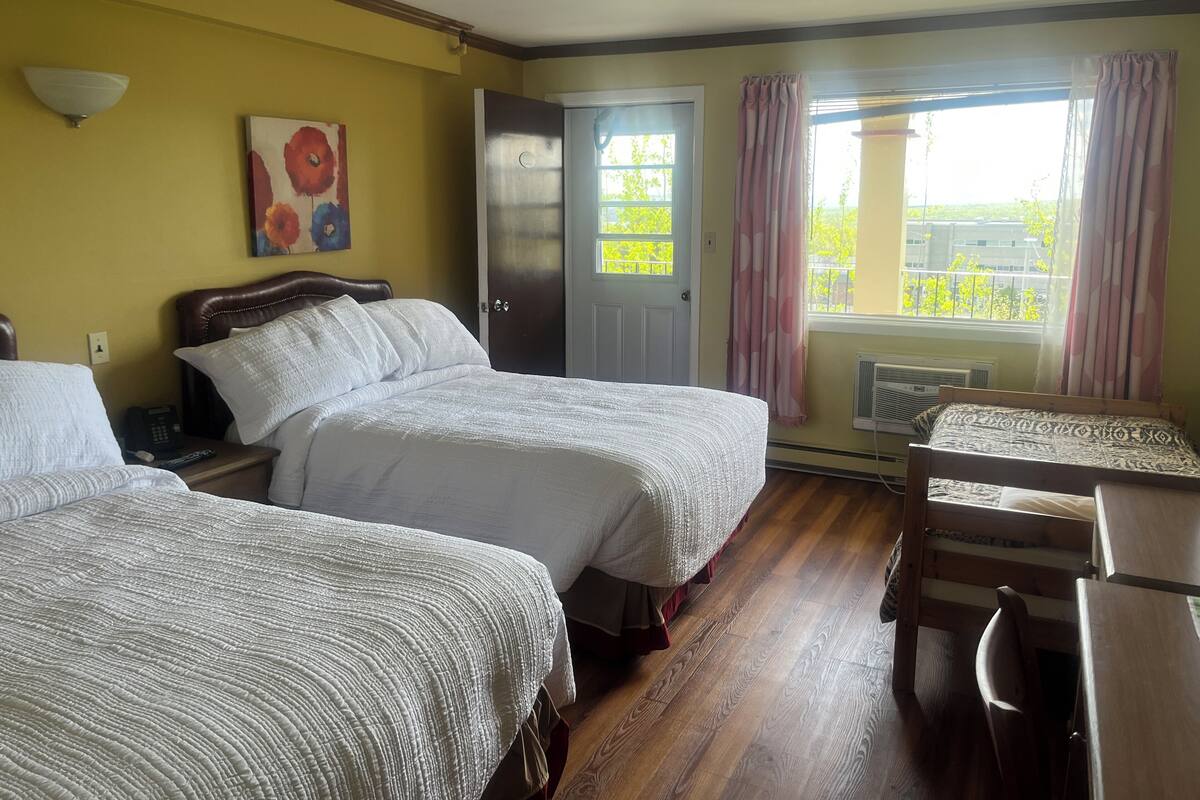 A hotel room with two beds, a desk, a chair, a painting, and a window with curtains.