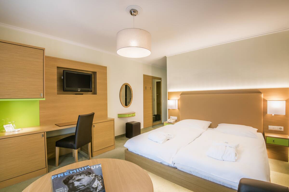 A hotel room with a bed, a desk, a chair, a television, and a mirror.