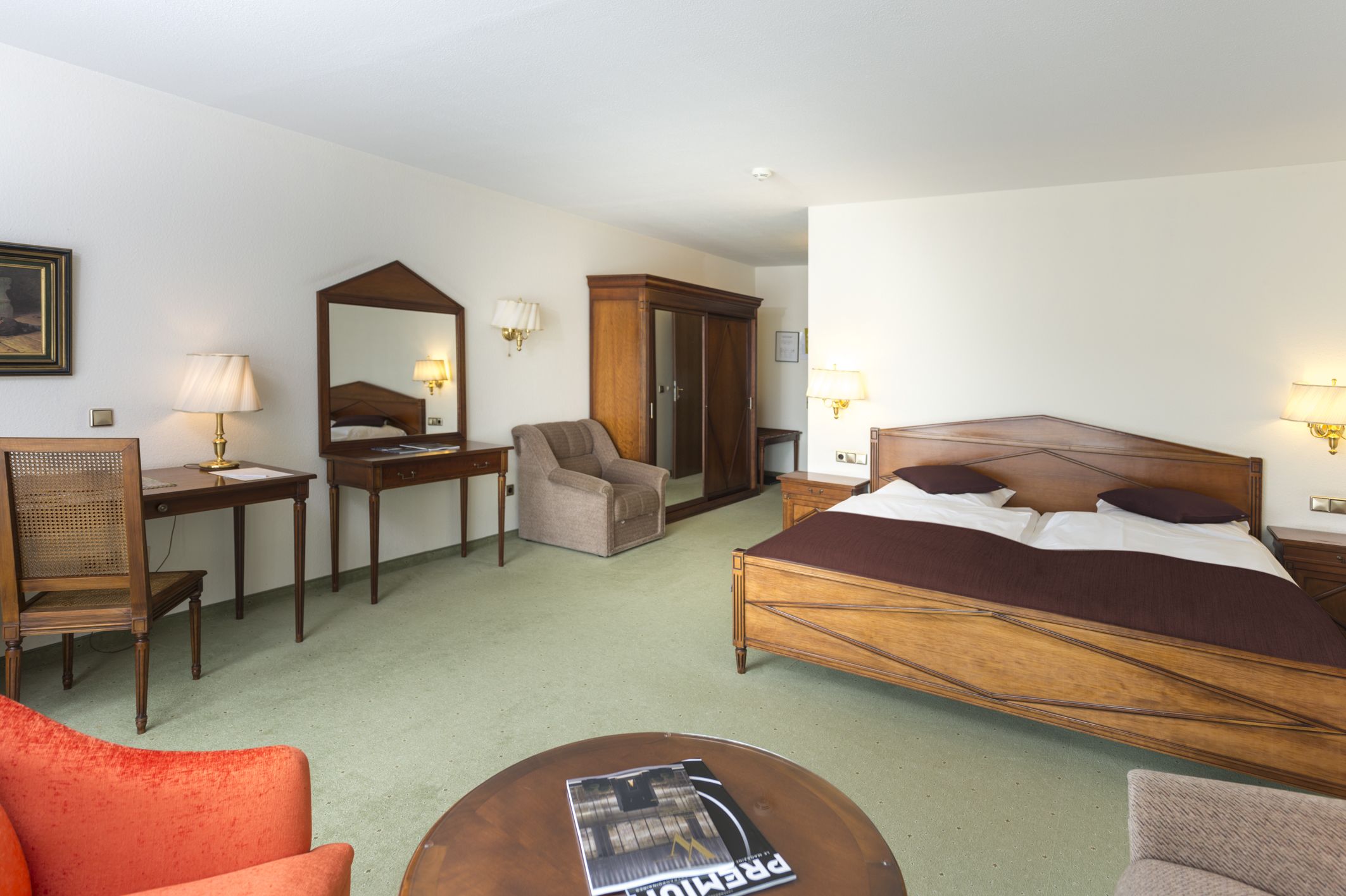 Una habitación de hotel con una cama grande, un escritorio, una silla, un armario y una mesita con una revista.