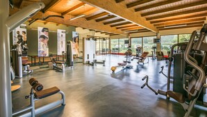 A spacious gym with various exercise equipment, large windows, and a wooden ceiling. - Hôtel Eden au Lac (Echternach)