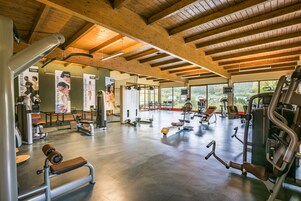 Un gimnasio espacioso con diversos equipos de ejercicio, amplias ventanas y techo de madera.
