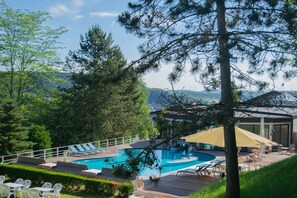 Una piscina con sillas de descanso y una terraza, rodeada de árboles y vistas a colinas.