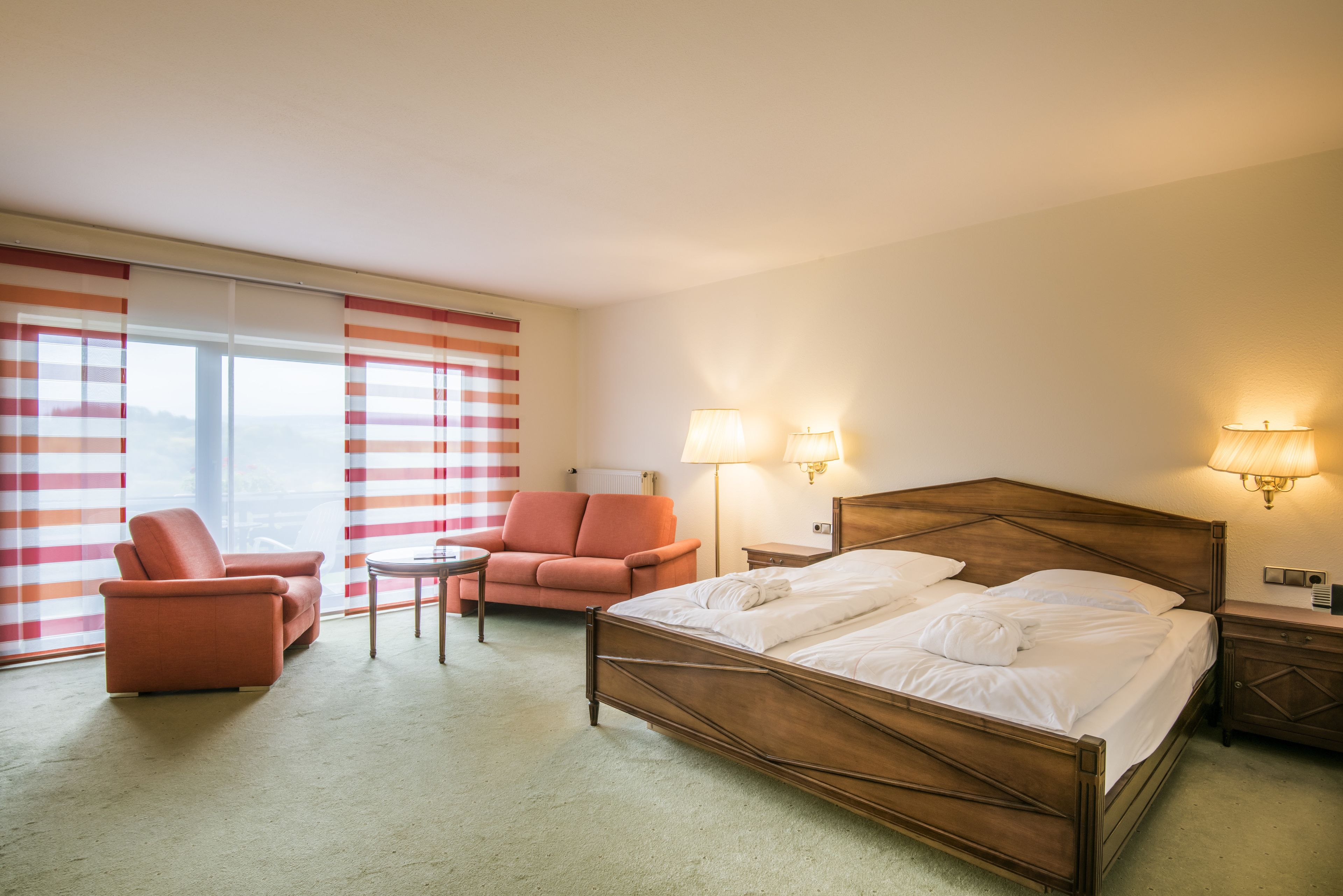 Una habitación de hotel con una cama, una silla, una mesita y dos lámparas.