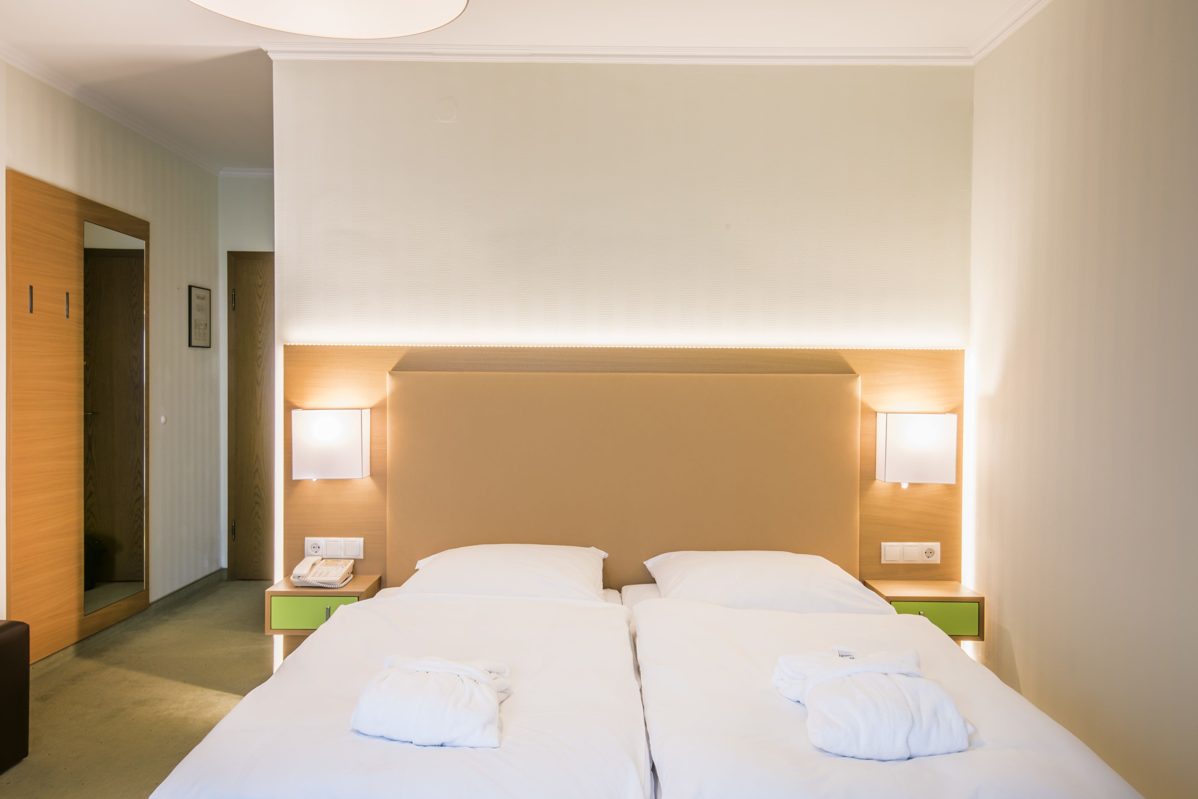 Quarto de hotel com duas camas, luminárias de cabeceira, um telefone e uma mesinha de cabeceira verde.
