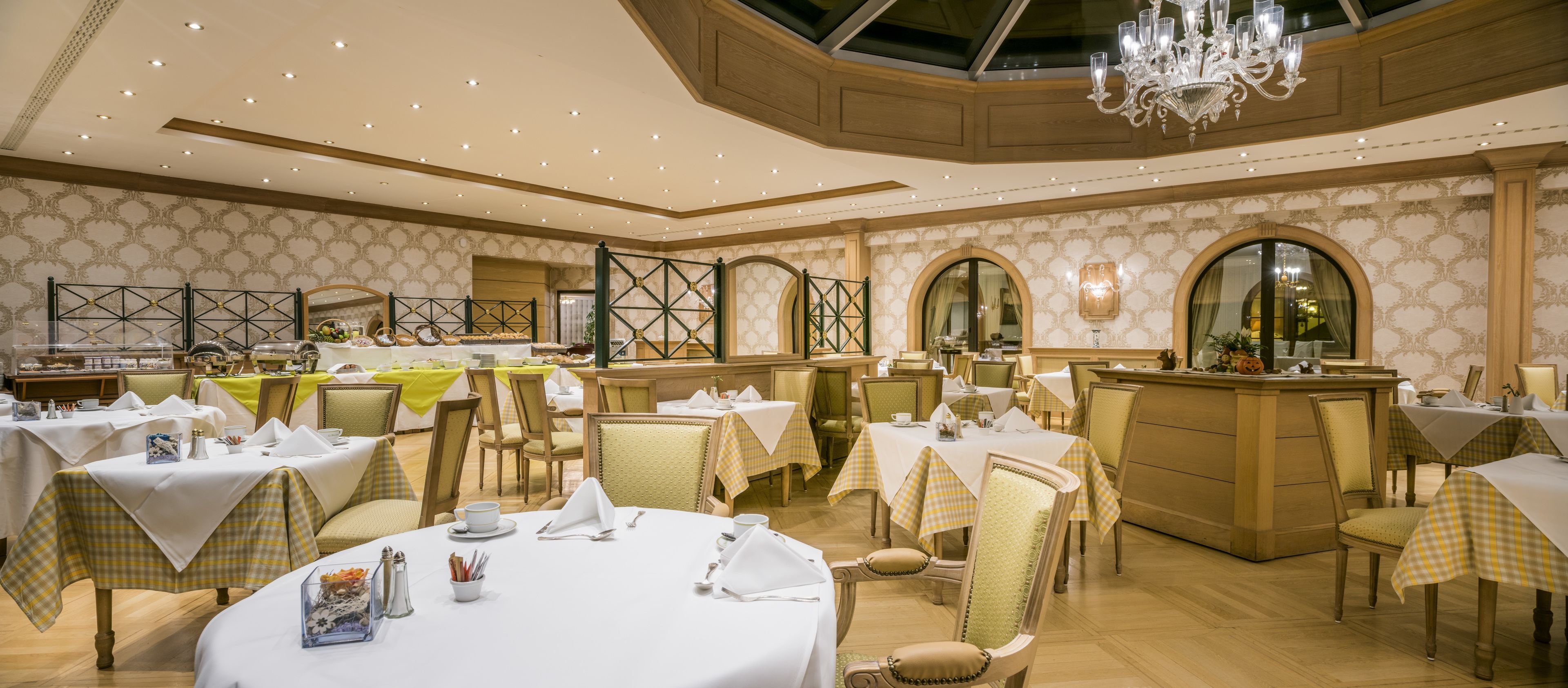 Uma sala de jantar com mesas redondas, toalhas xadrez e cadeiras clássicas.