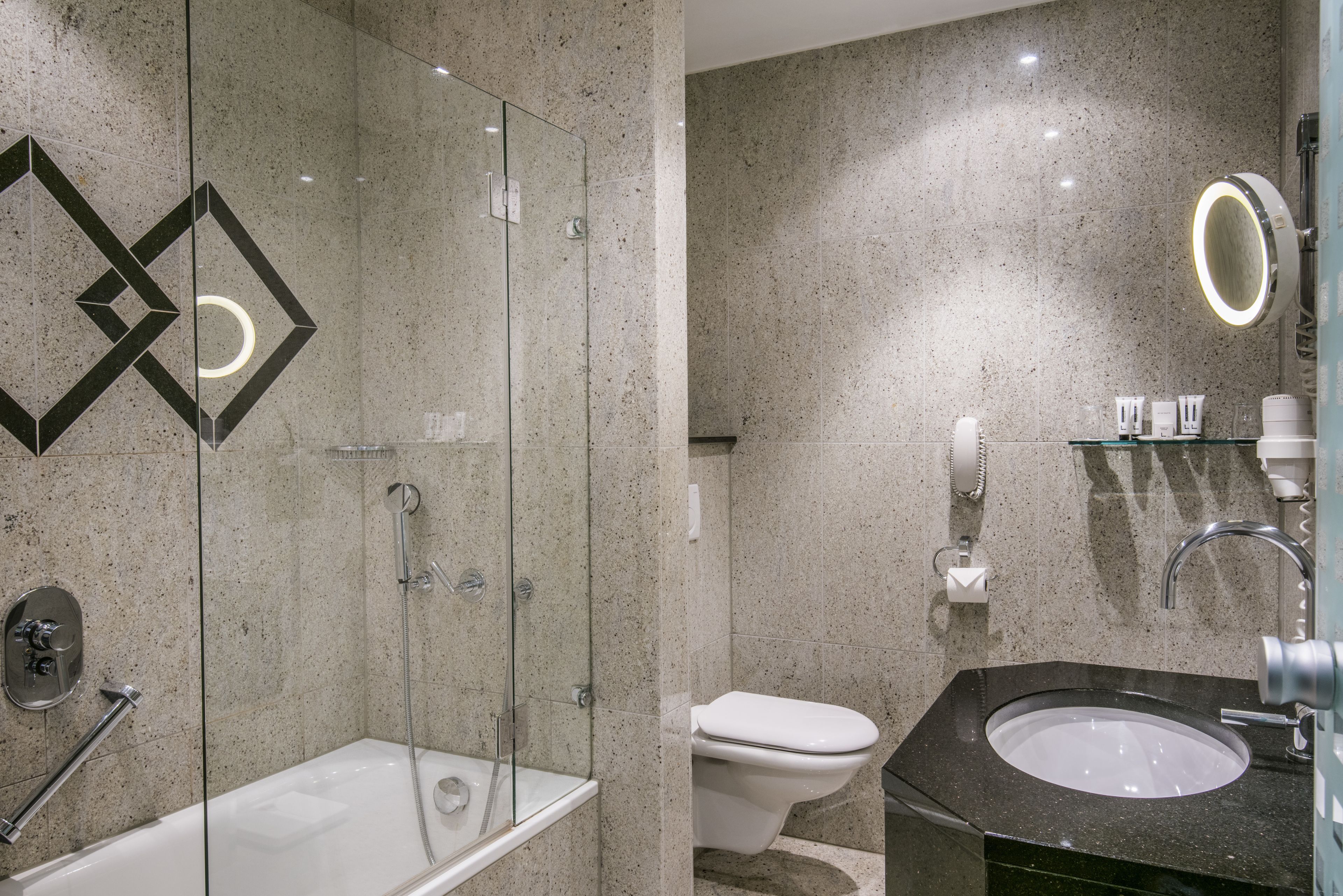 Un baño moderno con ducha envuelta en vidrio, bañera, inodoro y lavamanos con espejo.
