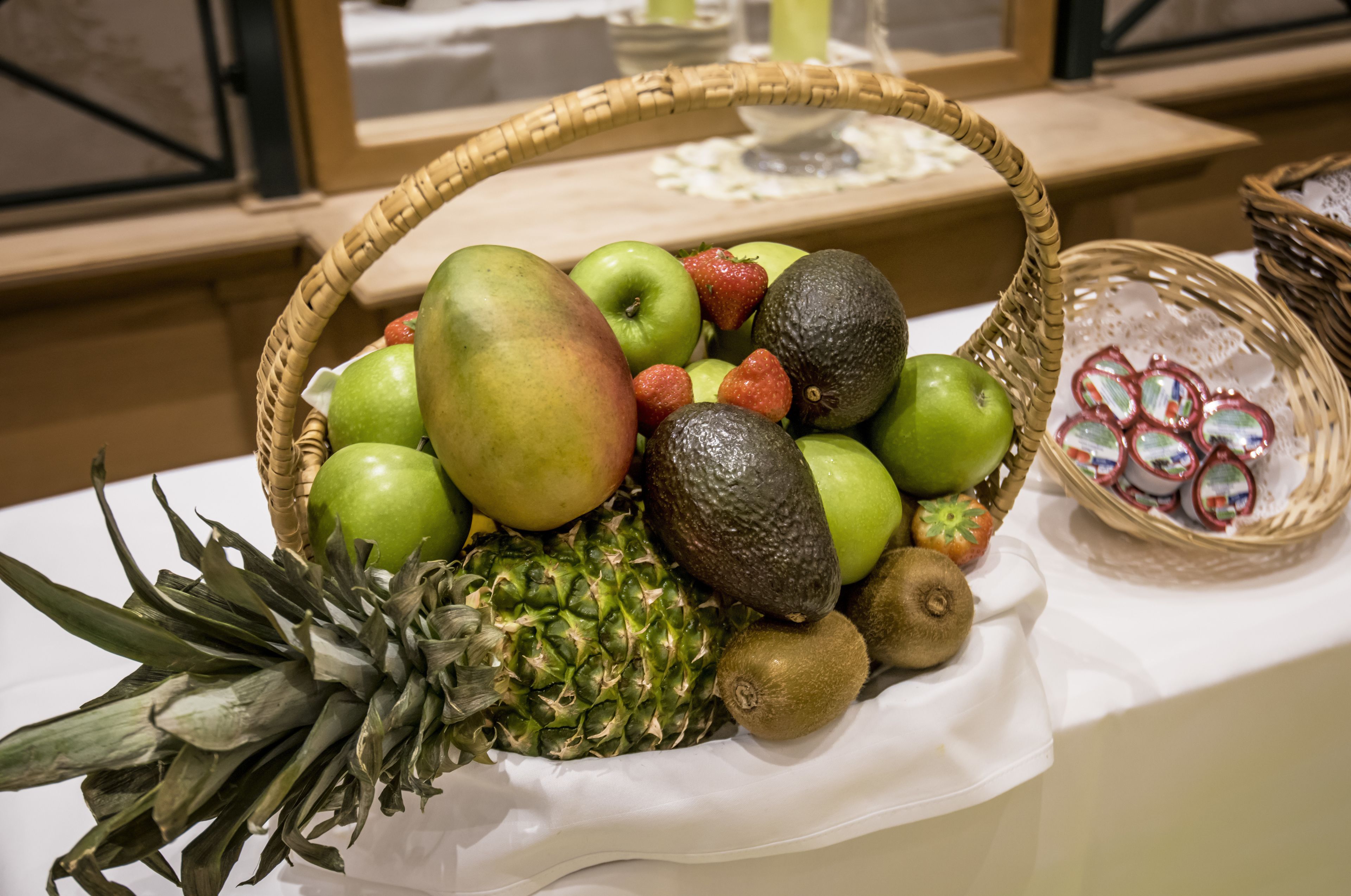 A fruit basket with apples, strawberries, and avocados on a table.