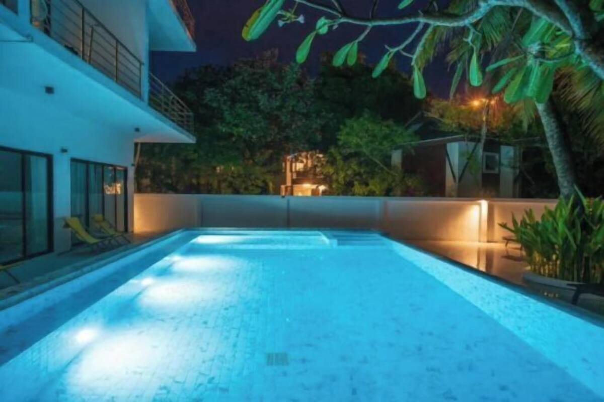 A swimming pool with a modern design, surrounded by a well-maintained garden and a building with large windows.