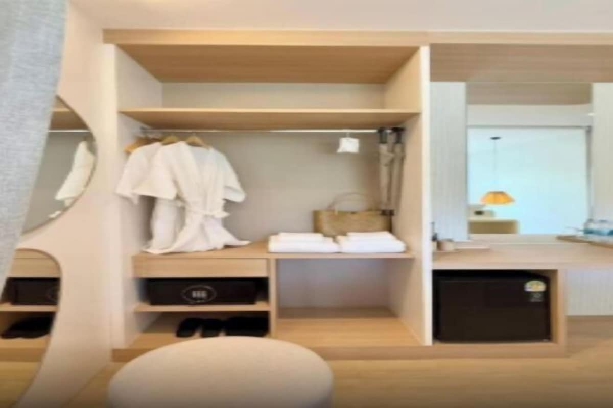 Une chambre d’hôtel moderne avec un plancher en bois, un placard intégré avec des cintres, un petit coin salon et un miroir.