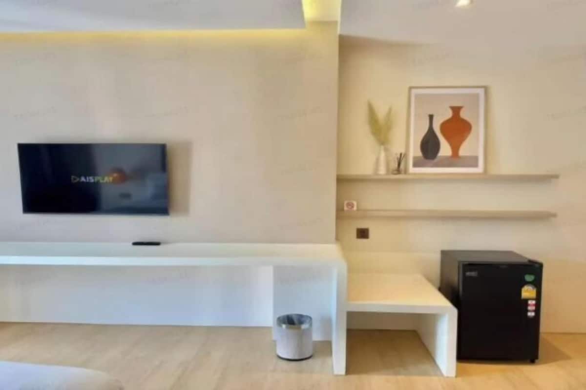 Une chambre d’hôtel moderne équipée d’un téléviseur à écran plat, d’un banc blanc, d’une petite poubelle et d’un réfrigérateur noir.