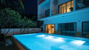 A modern two-story building with a swimming pool, outdoor seating, and a balcony.
