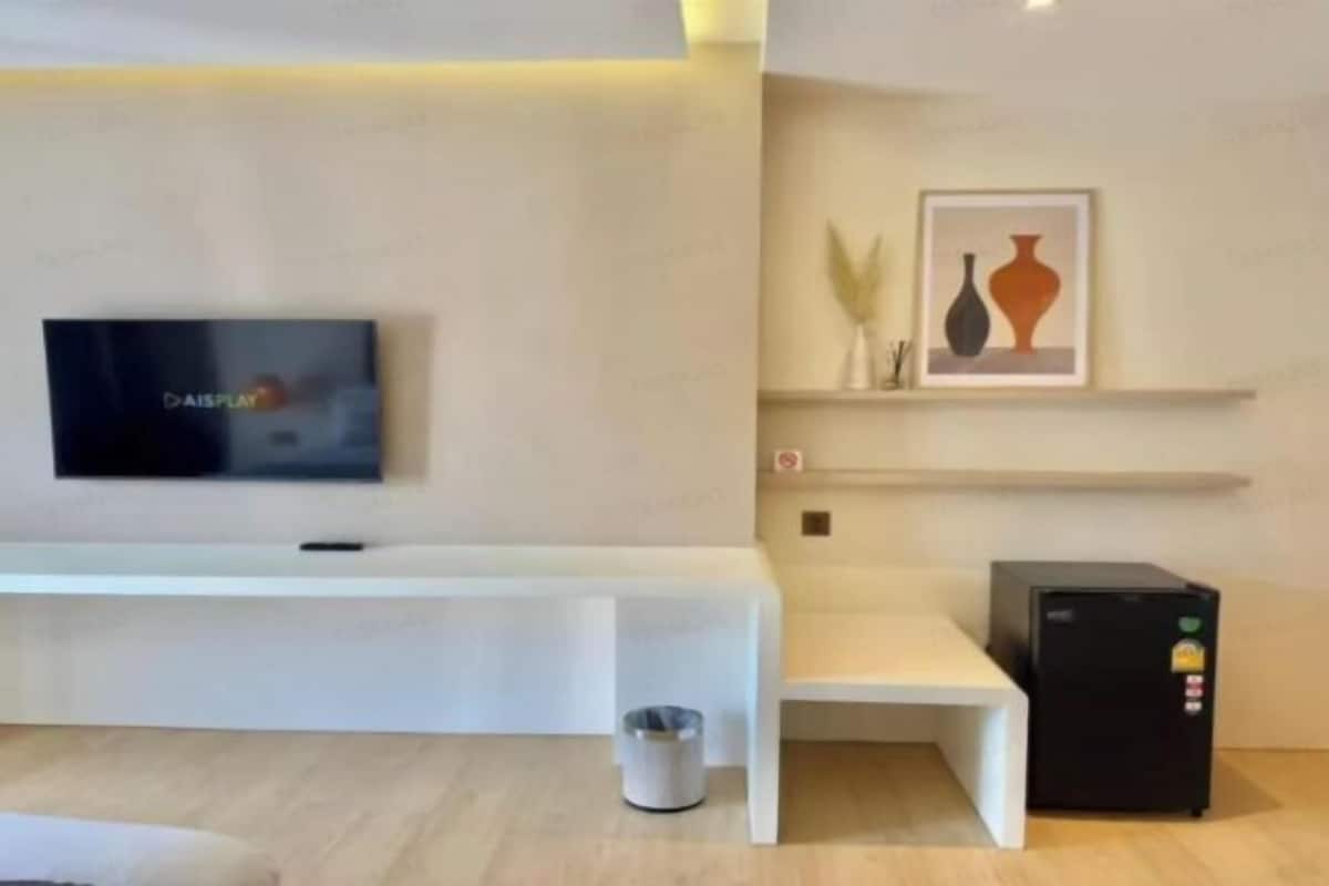 Un salon moderne avec un téléviseur à écran plat, un banc blanc, une petite poubelle, un réfrigérateur et une œuvre d’art encadrée accrochée au mur.