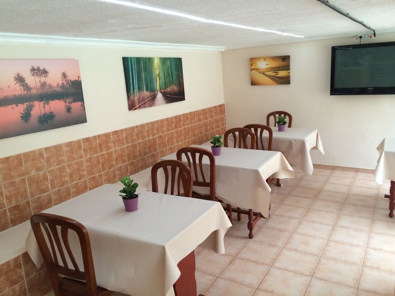 Un comedor con mesas y sillas, suelo de baldosas y obras de arte colgadas en la pared.