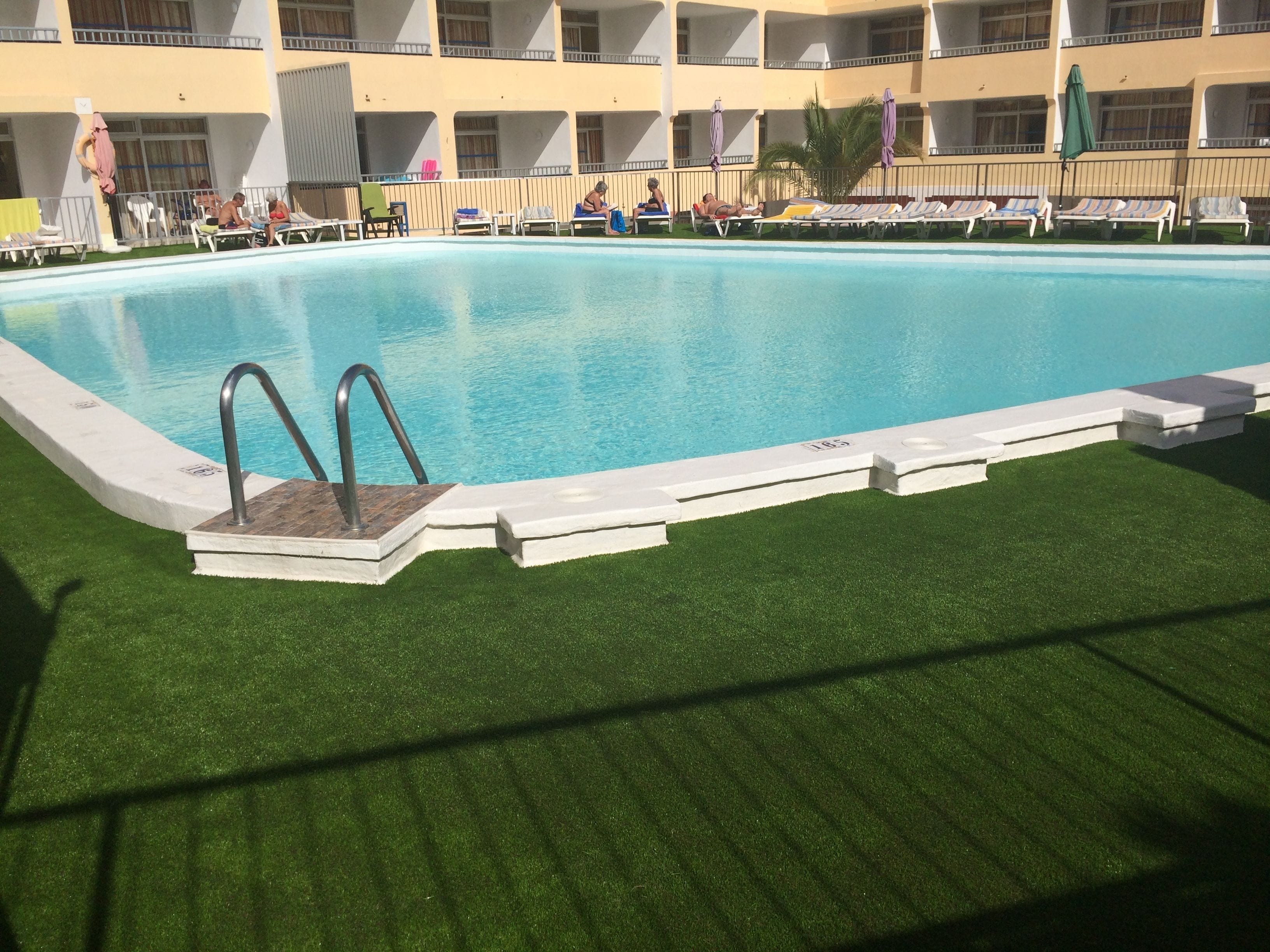 A swimming pool with a wooden deck and metal ladder, surrounded by lounge chairs and umbrellas.