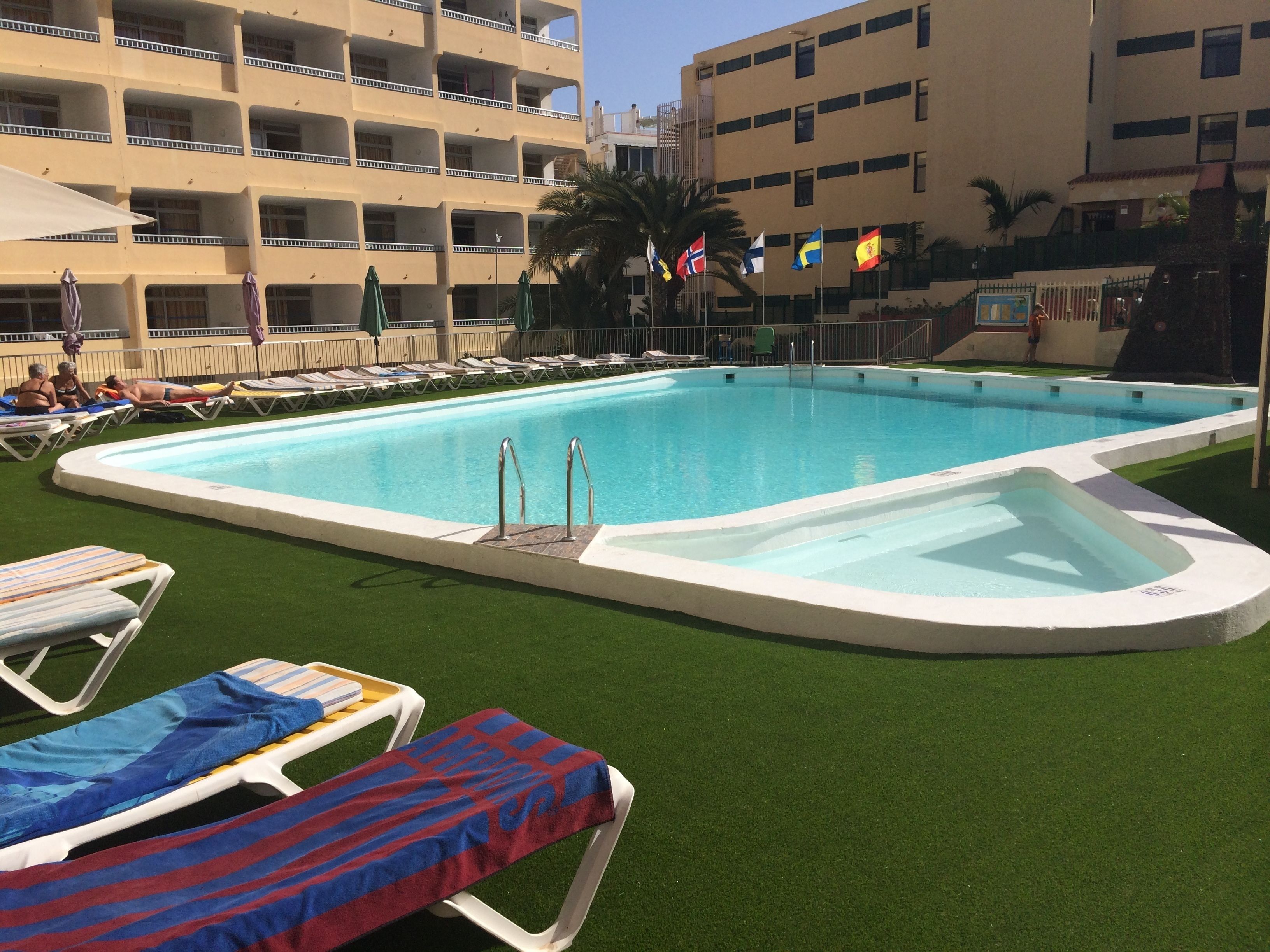 Una piscina con numerosas tumbonas y un pequeño jacuzzi.