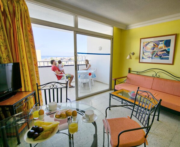Un balcón con una mesa para desayunar, un sofá y un televisor.