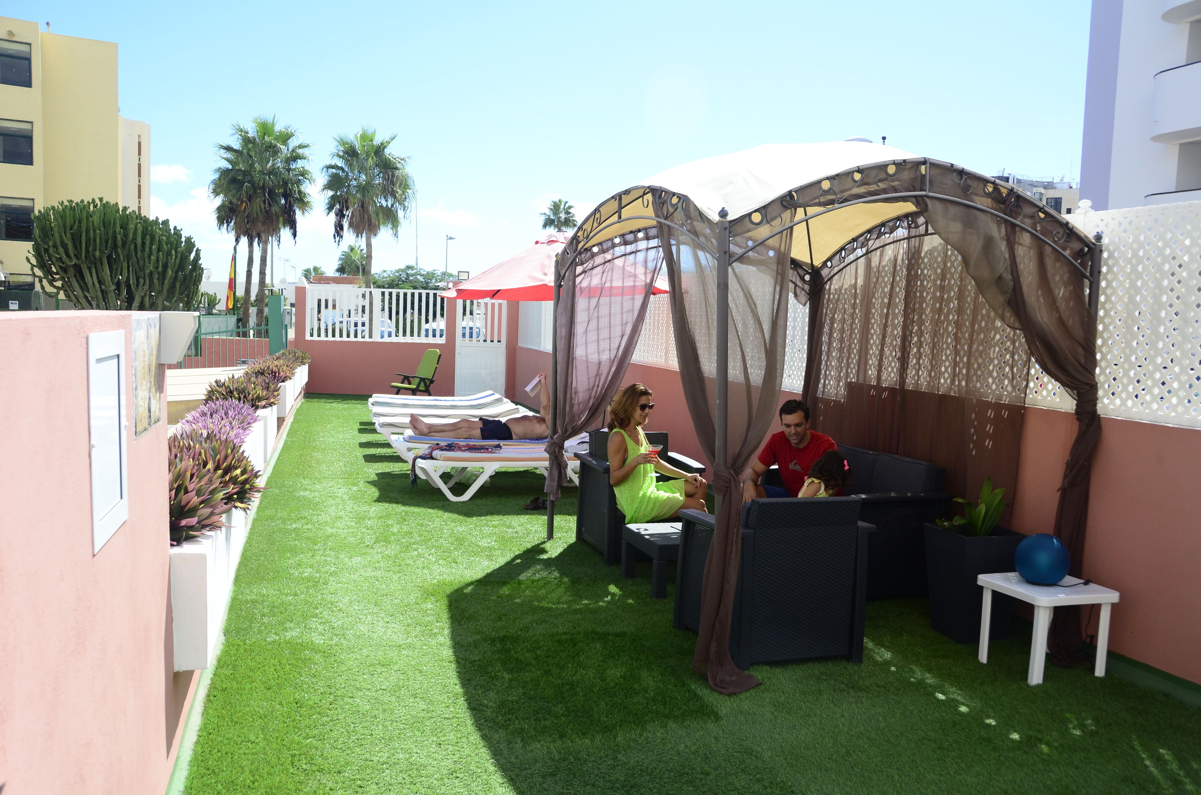 An outdoor patio with artificial grass, lounge chairs, and a shaded area with a canopy.