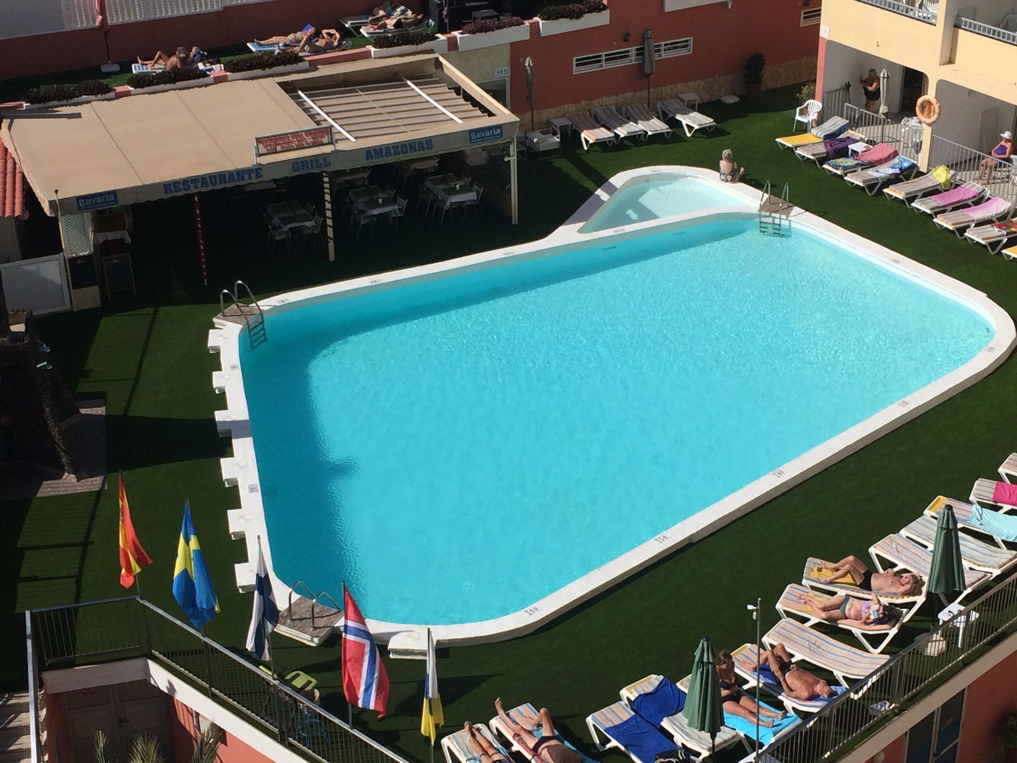 An outdoor swimming pool with lounge chairs and flags.