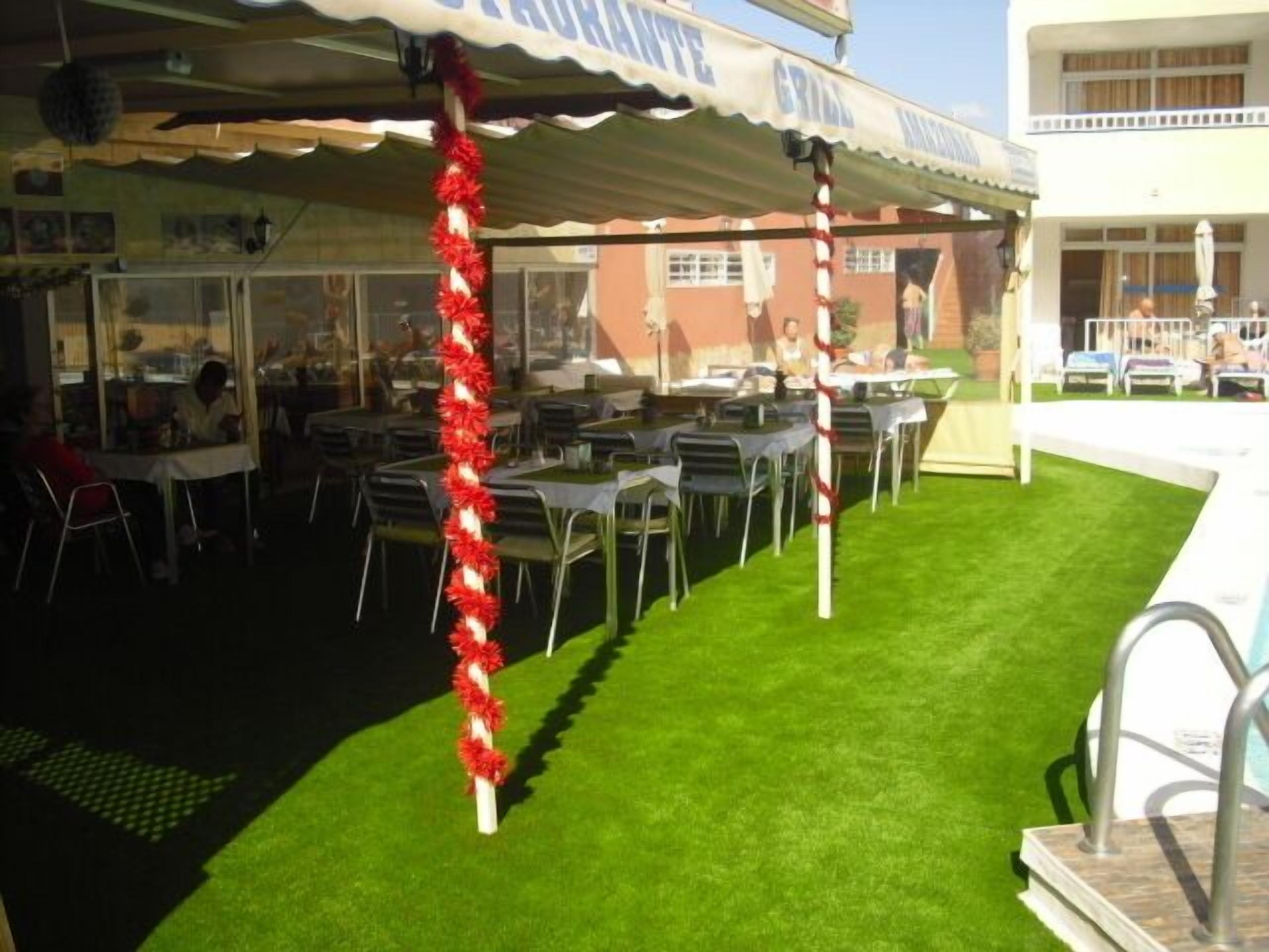 An outdoor dining area with tables and chairs, a grassy lawn, and a building in the background.