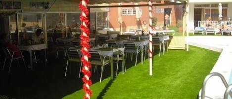 An outdoor dining area with tables and chairs, a grassy lawn, and a building in the background.