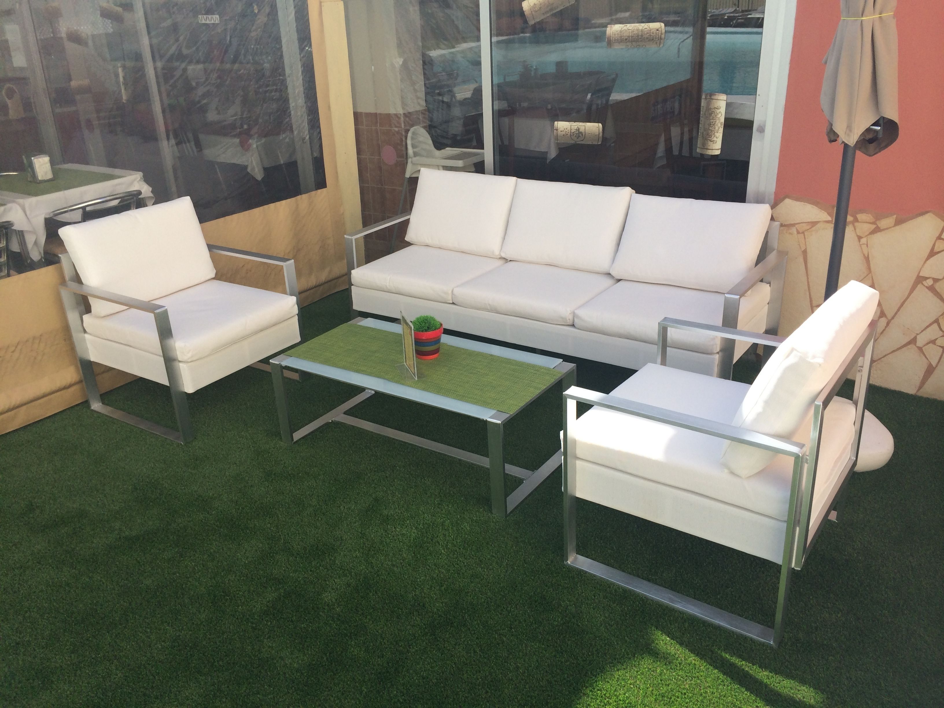 A modern outdoor seating area with a white sofa, two white armchairs, and a glass coffee table.