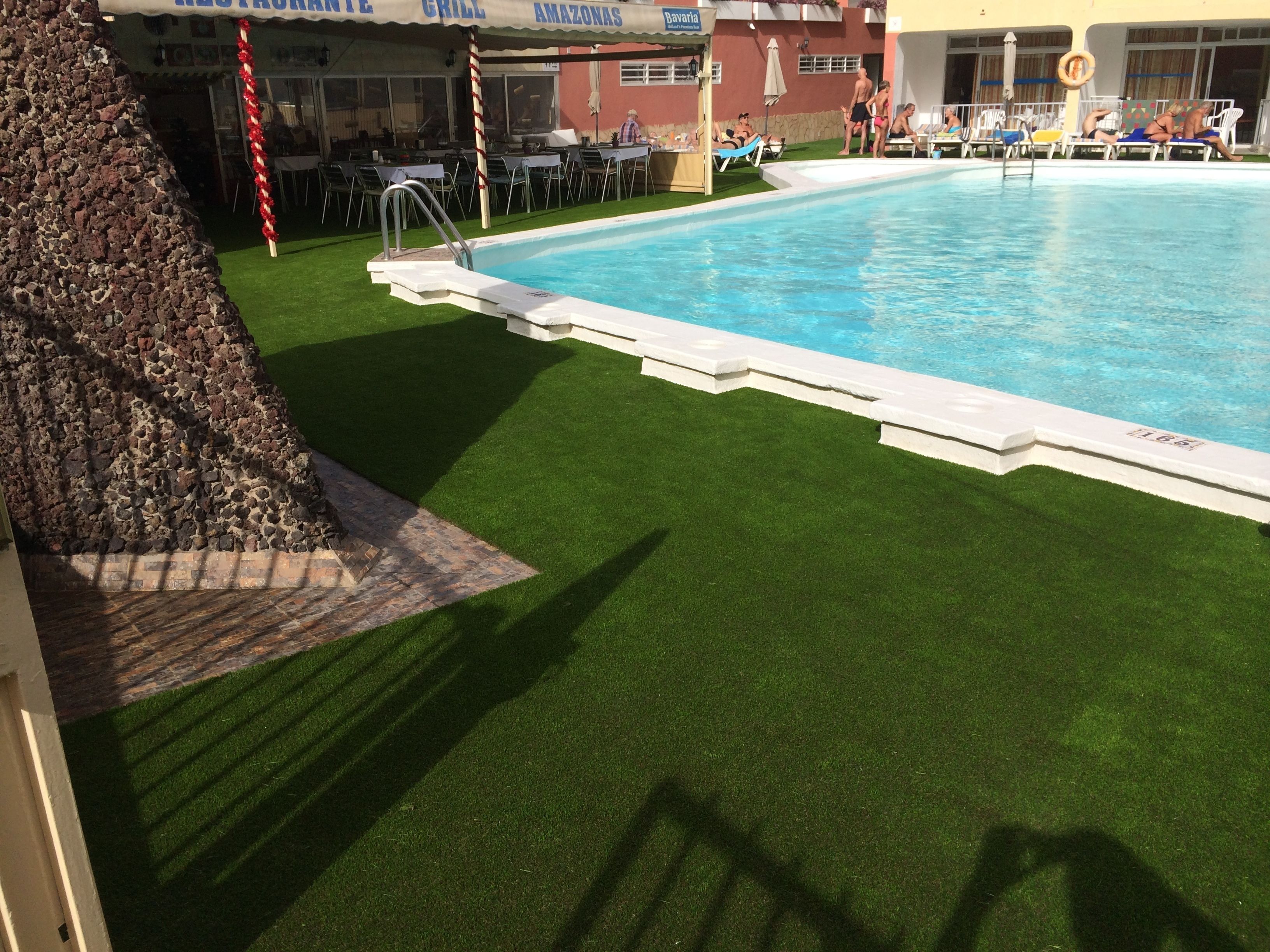 Una piscina con pared de piedra y césped artificial.