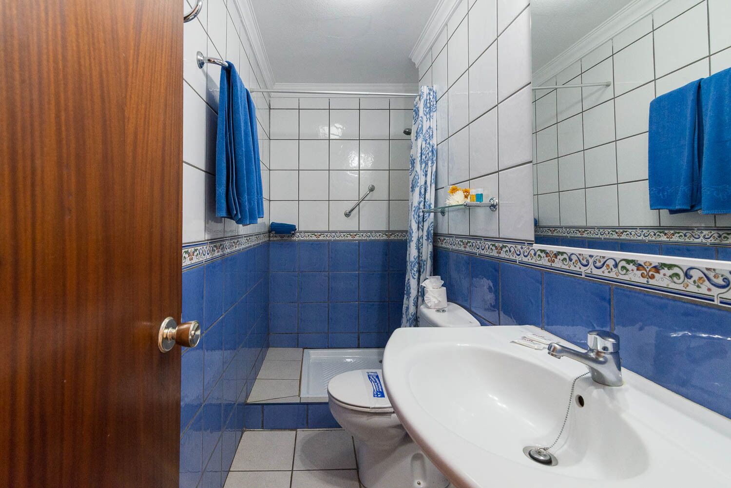 A bathroom with blue tiles, a white sink, a toilet, and a shower area.