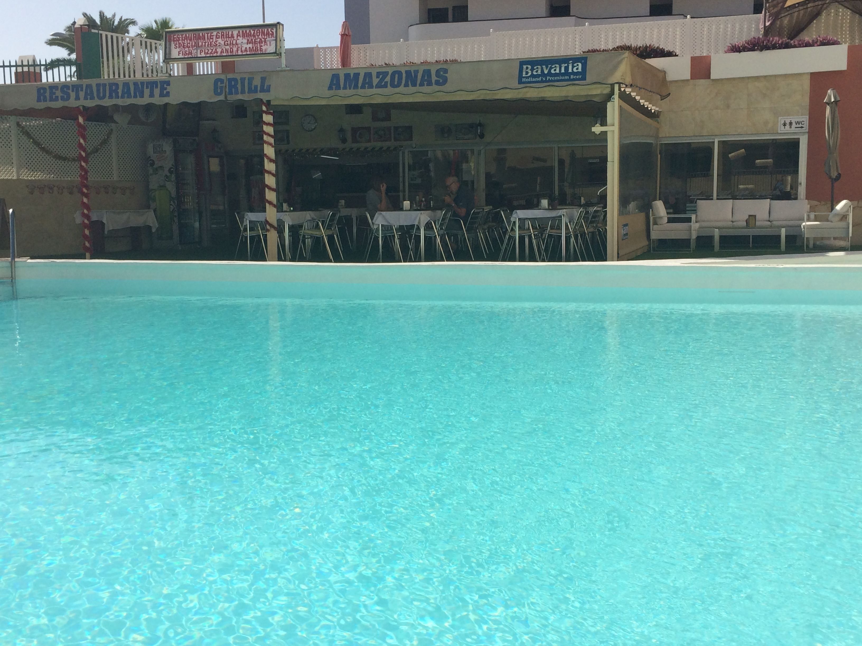 A swimming pool with a restaurant named 'Amazonas' and 'Bavaria' in the background.