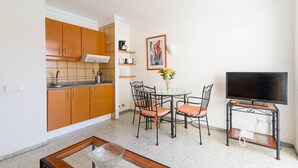 Ein kompakter Wohnbereich mit Küchenzeile, Essbereich und Fernseher auf einem Schrank.
