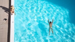 Ein Schwimmbad mit klarem, blauem Wasser, einer gefliesten Liegefläche und einer darin schwimmenden Person.