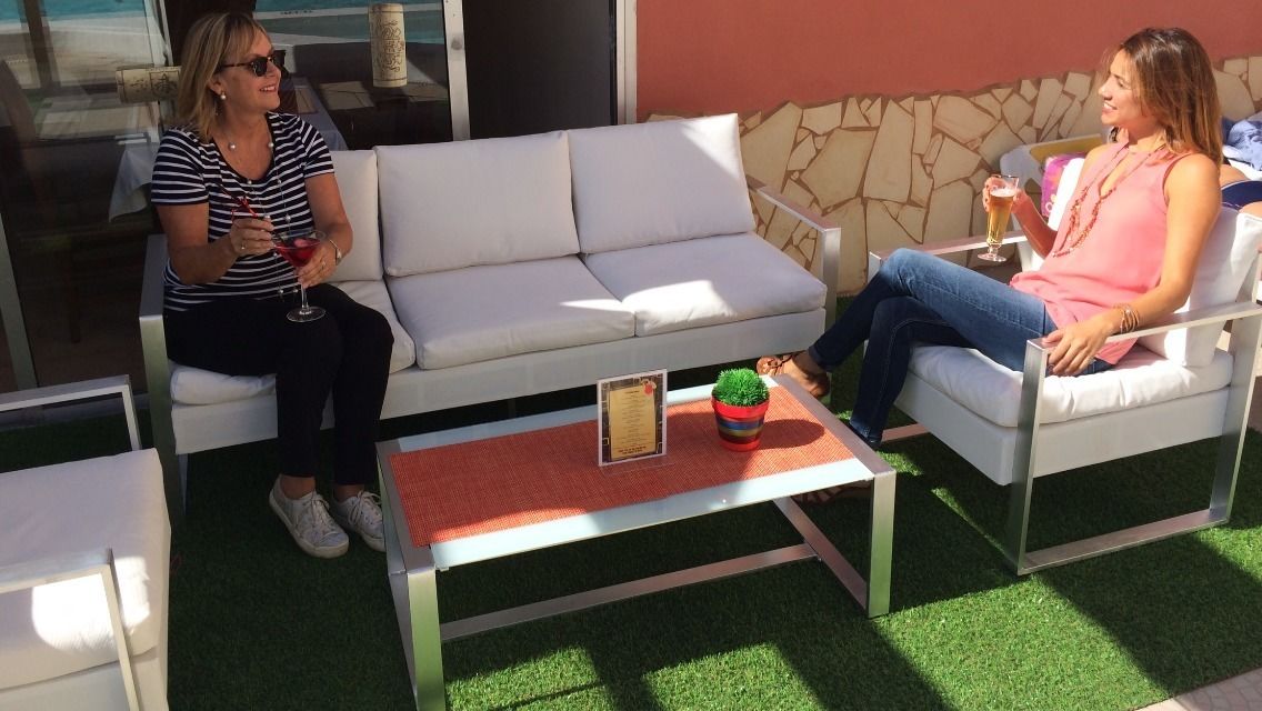 Dos personas sentadas en sofás blancos al aire libre con una pequeña mesa entre ellas.