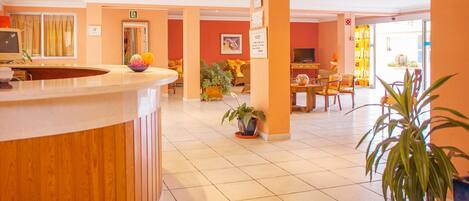 A hotel lobby with a reception desk, seating area, and a television.
