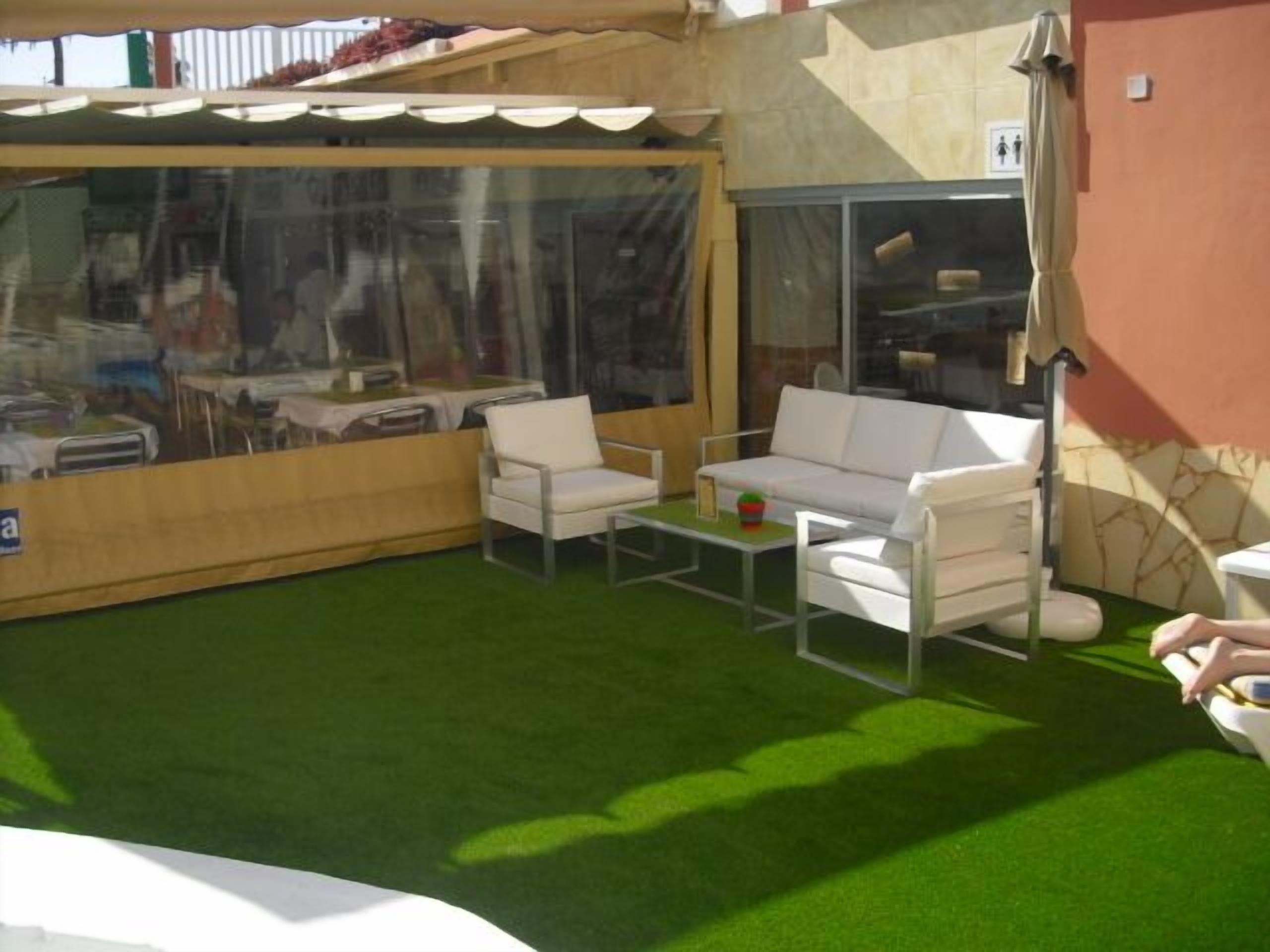 A patio area with a green artificial turf, white outdoor furniture, and large windows.