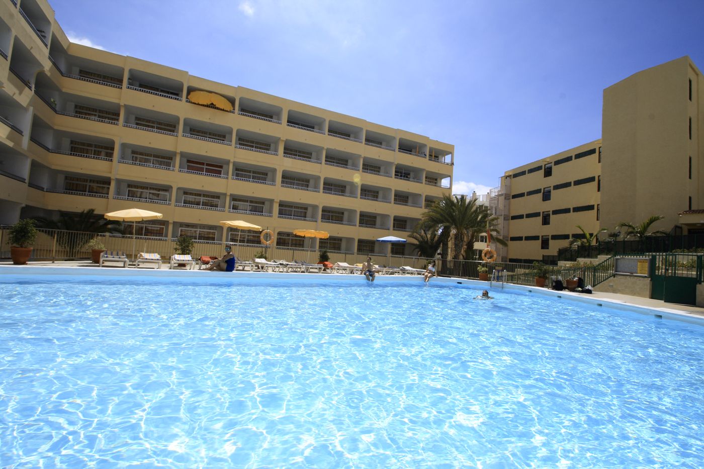 A hotel pool area with multiple levels of balconies, sun loungers, and umbrellas.