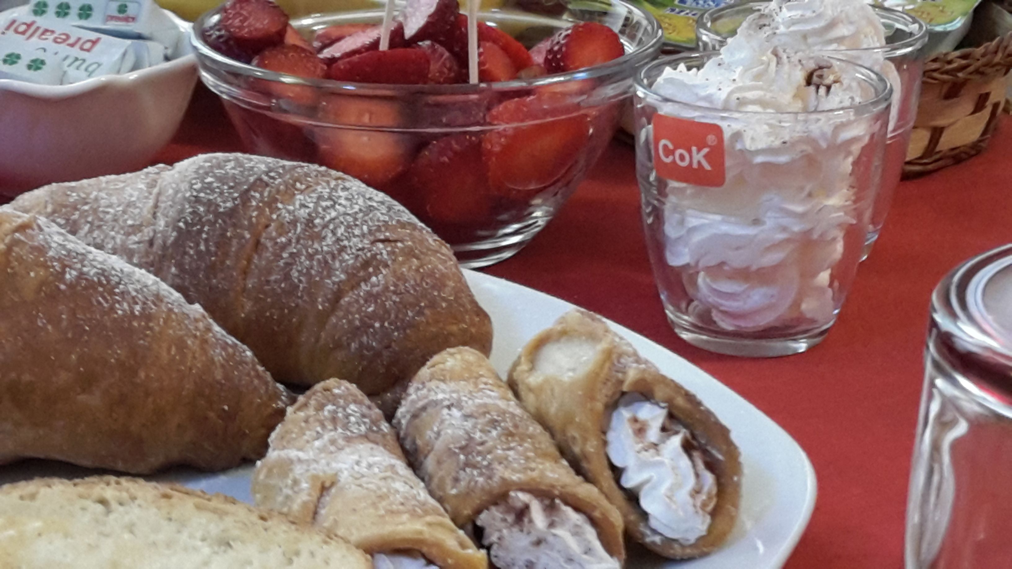 Una mesa con pasteles, un bol de fresas y un vaso de bebida con etiqueta.