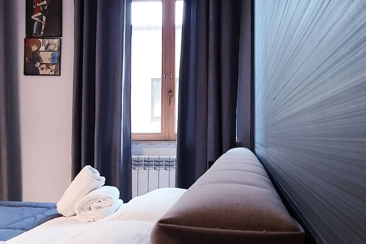 Quarto de hotel com cama, janela com cortinas, radiador e obras de arte na parede.
