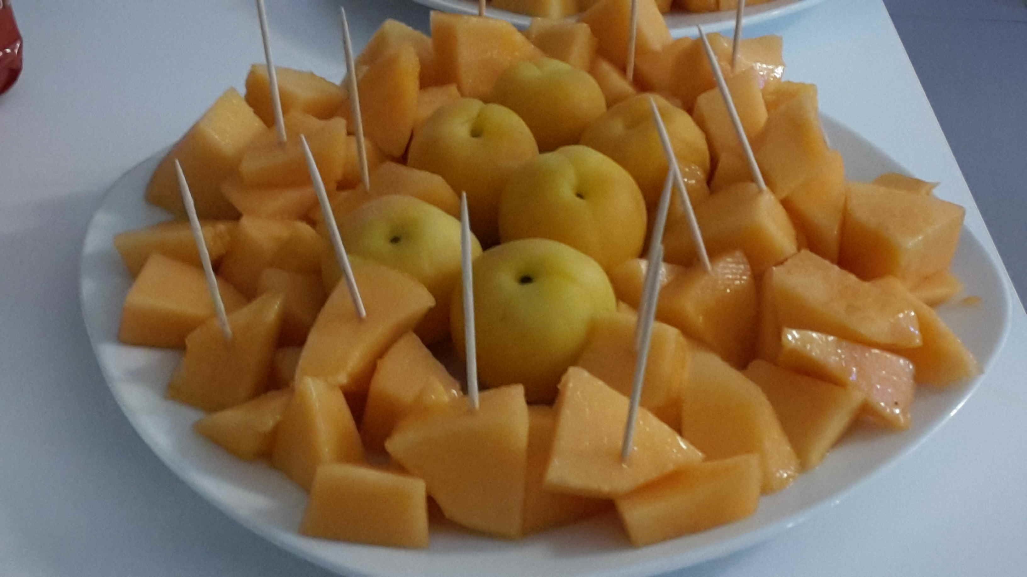 Ein Teller mit Cantaloupe-Melone und Äpfeln, garniert mit Zahnstochern.