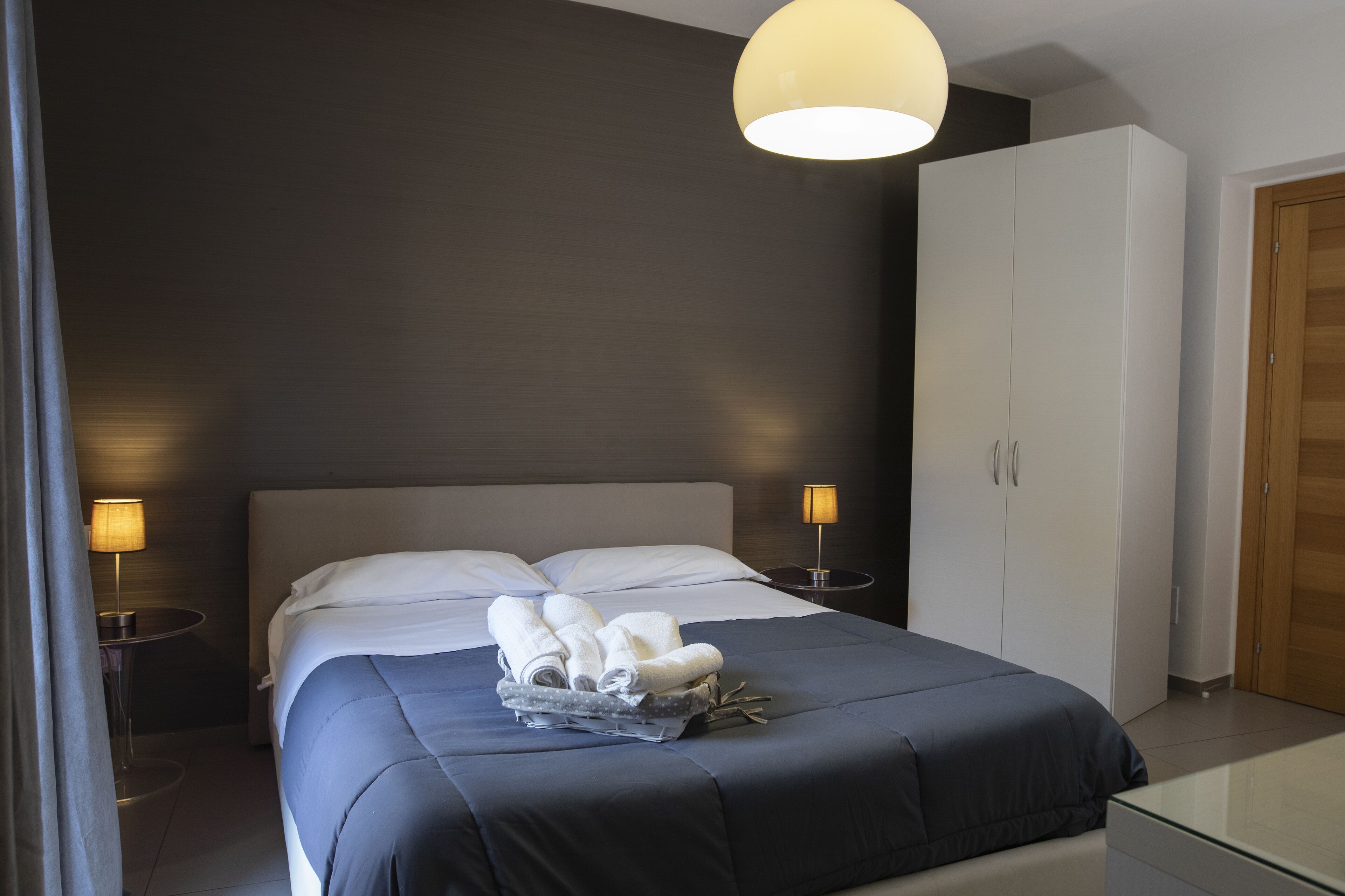 Une chambre à coucher moderne avec un grand lit, une table de chevet, une lampe et une armoire.