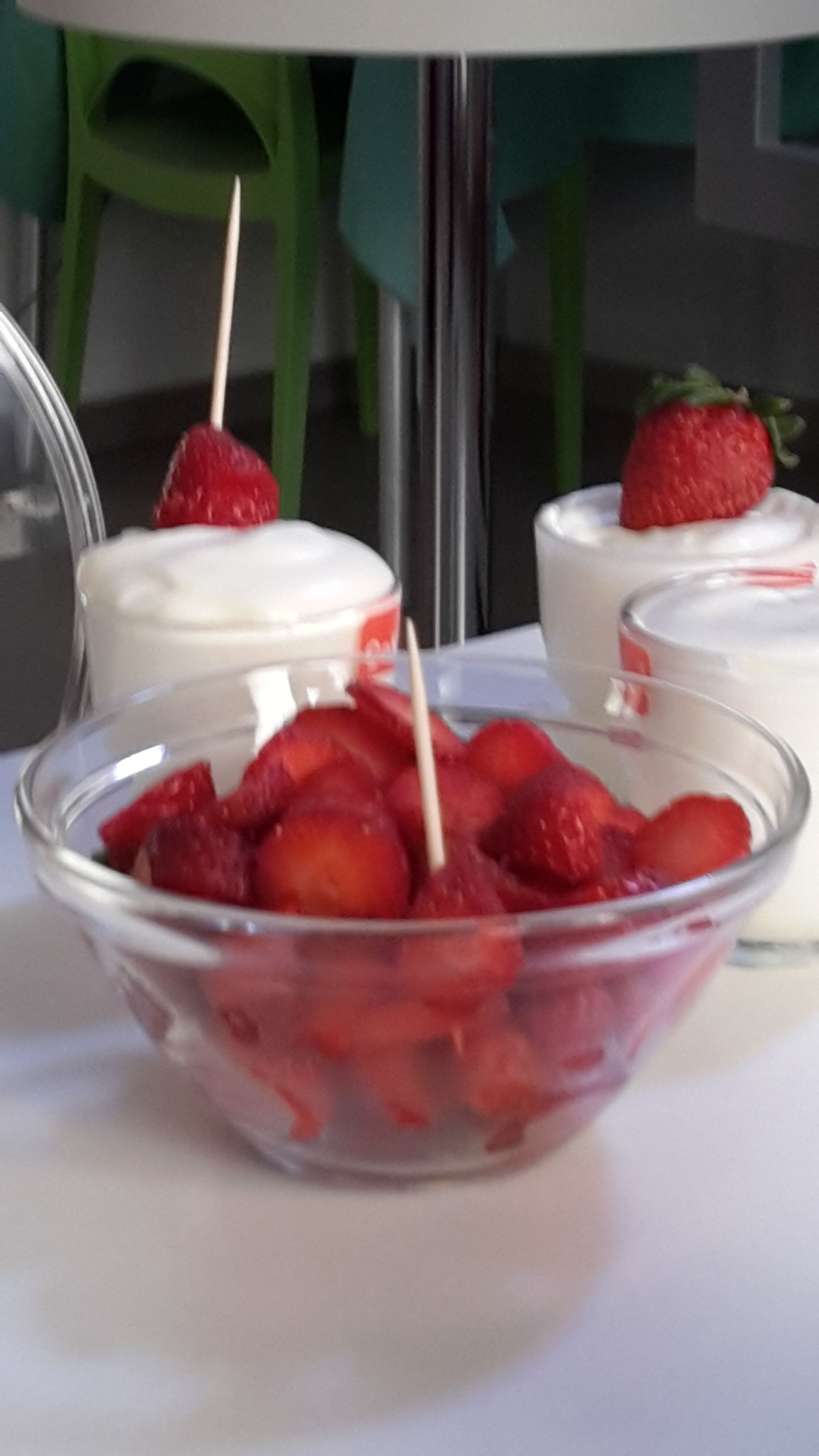 Un tazón de vidrio transparente lleno de fresas y un palillo, sobre una superficie blanca.
