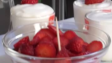 Un tazón de vidrio transparente lleno de fresas y un palillo, sobre una superficie blanca.