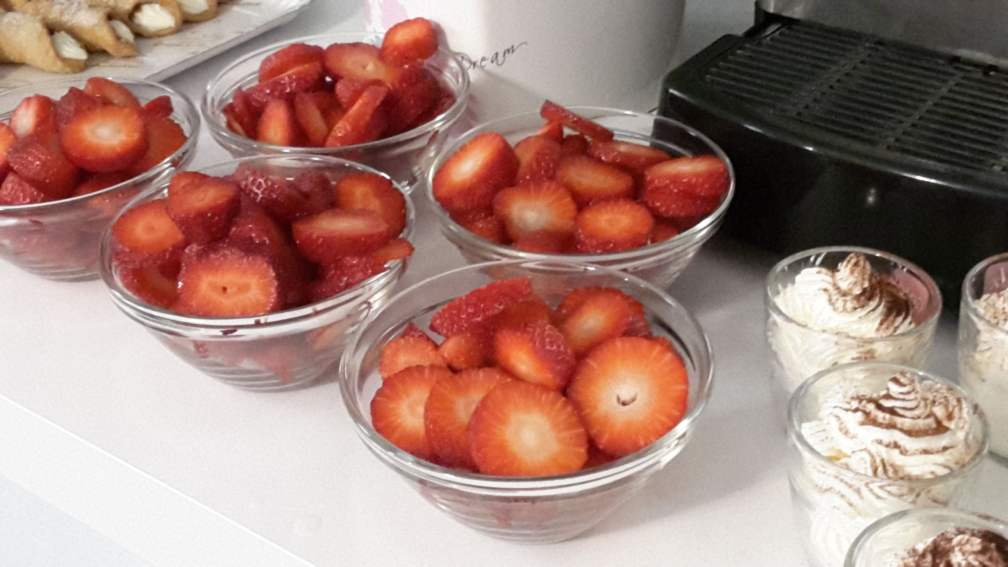 Bowls of sliced strawberries and whipped cream desserts on a countertop.