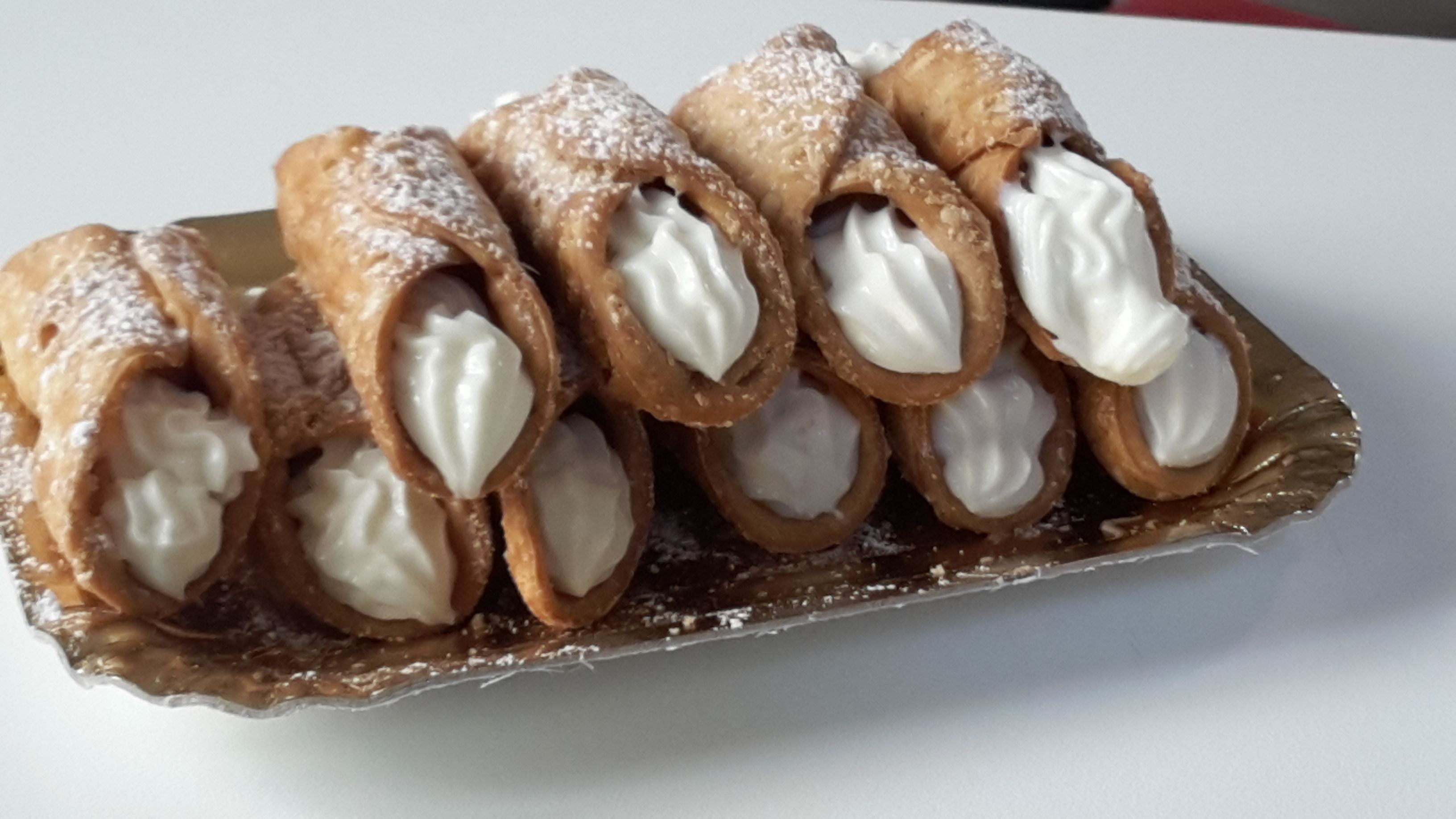 Una bandeja de cannoli rellenos de crema, espolvoreados con azúcar glas.