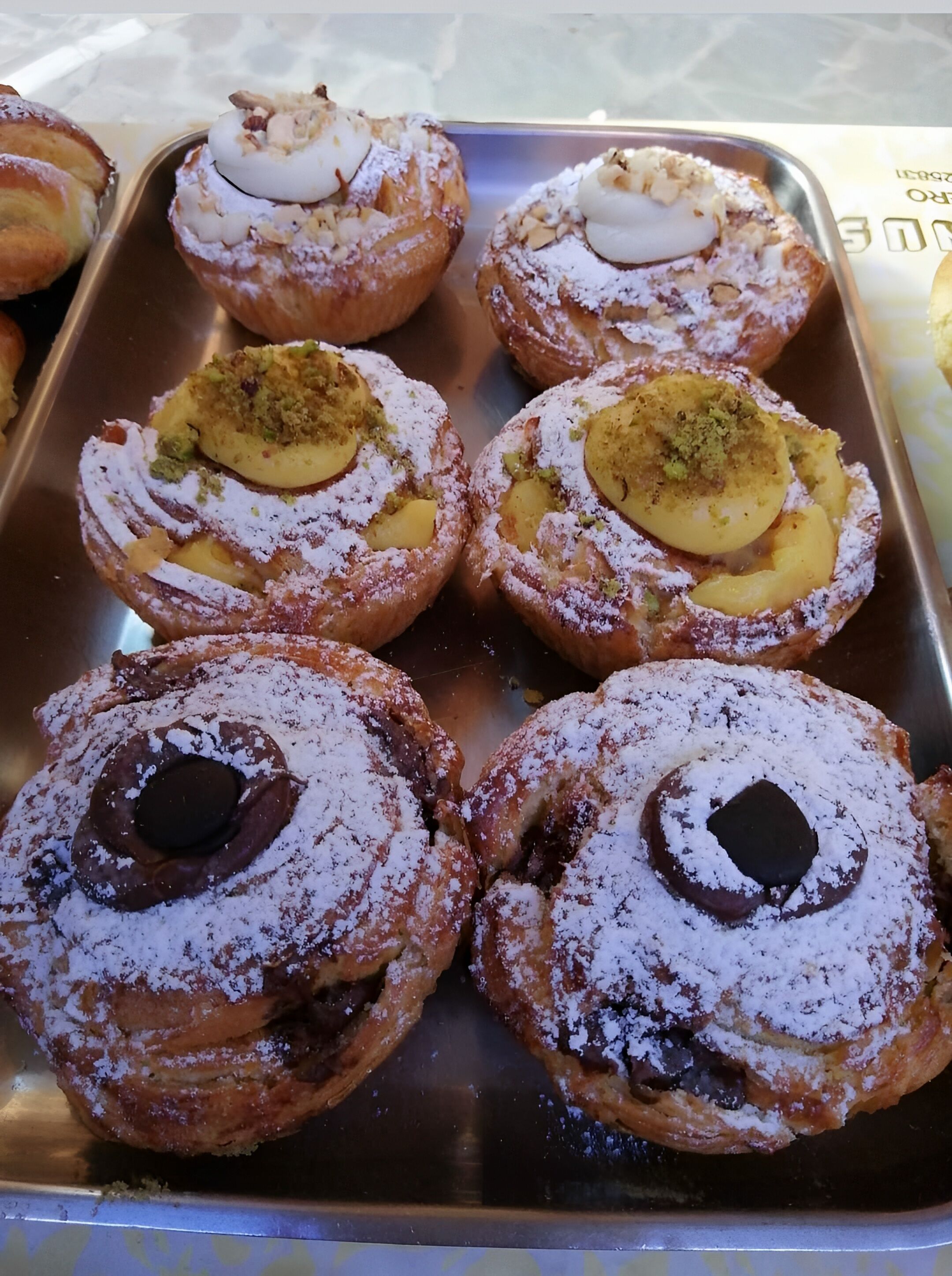 A tray of assorted pastries, including doughnuts and filled pastries, dusted with powdered sugar.