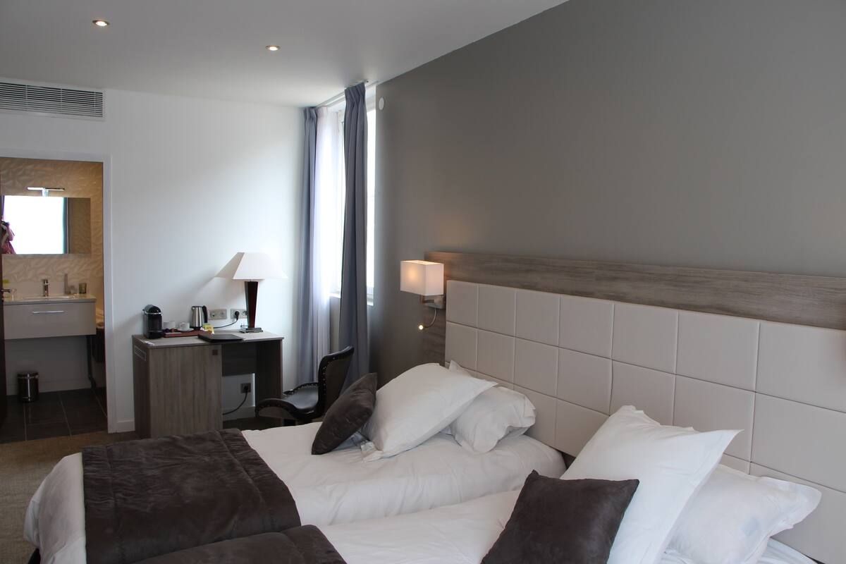 A hotel room with a bed, a desk, a chair, a lamp, and a window with curtains.
